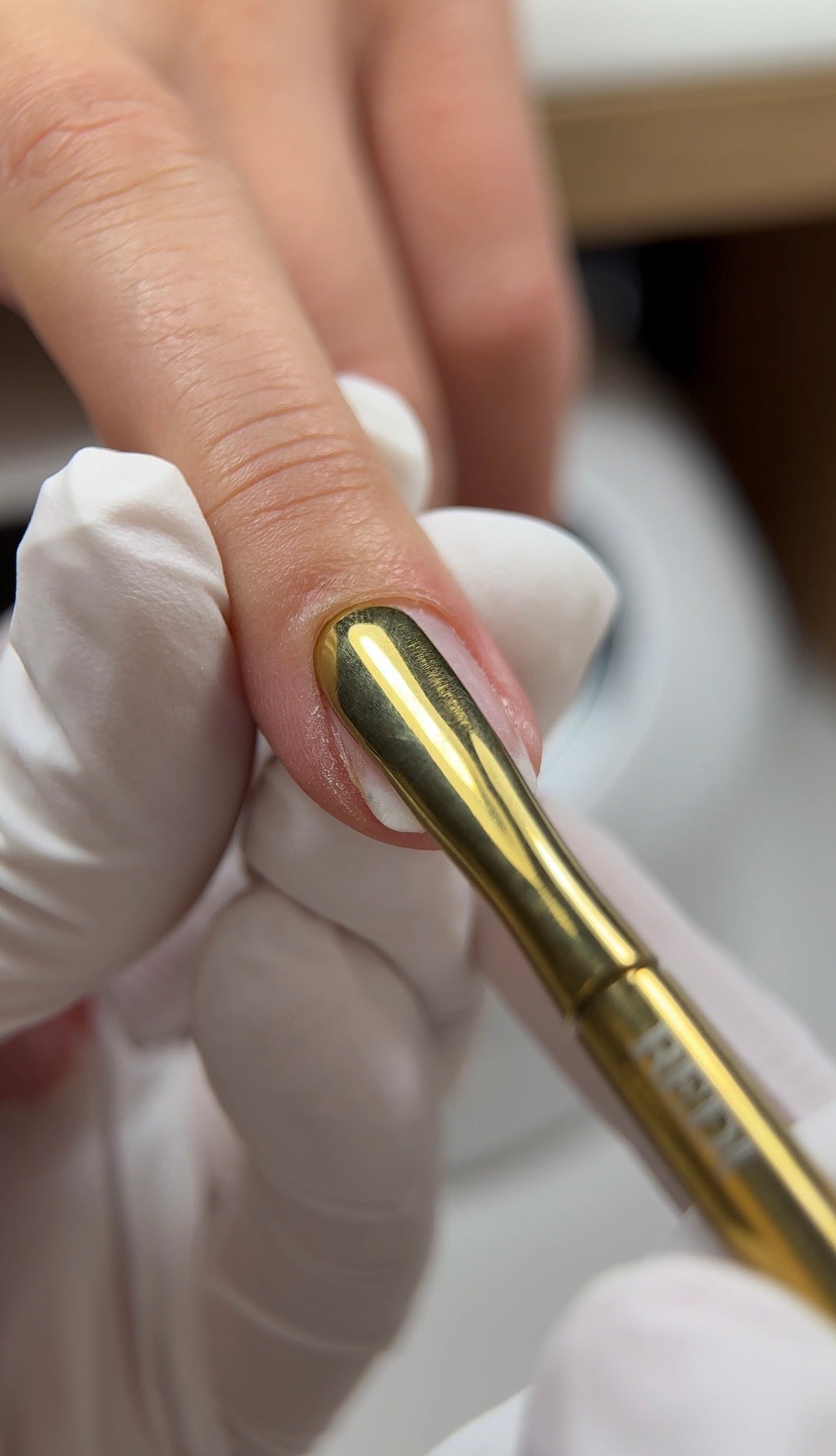 Close-up of a hand applying nail treatment with a gold tool, showcasing clean nail care and precision.