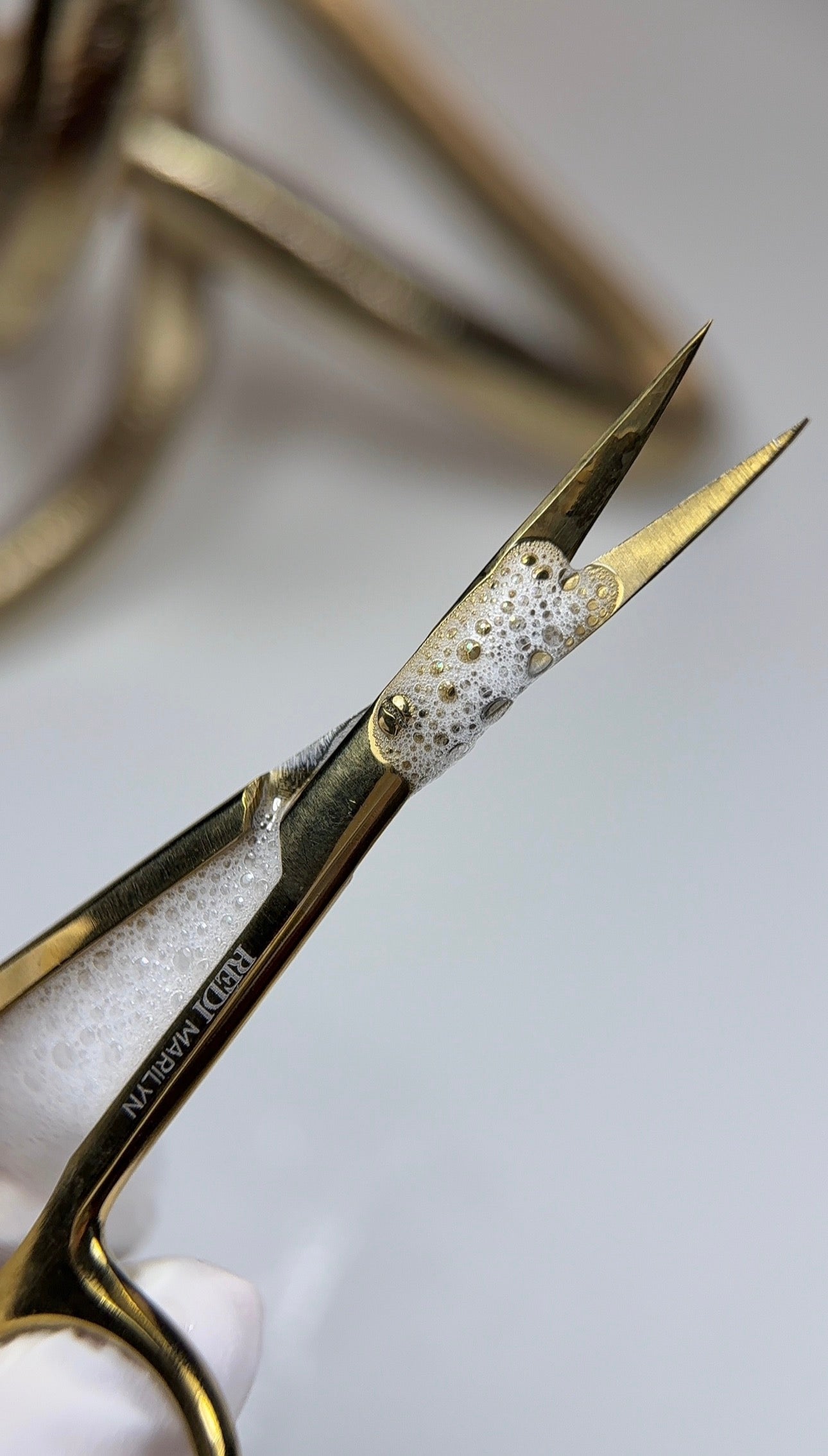 Gold surgical scissors with soap bubbles on blades, ideal for precision cutting and hygiene.